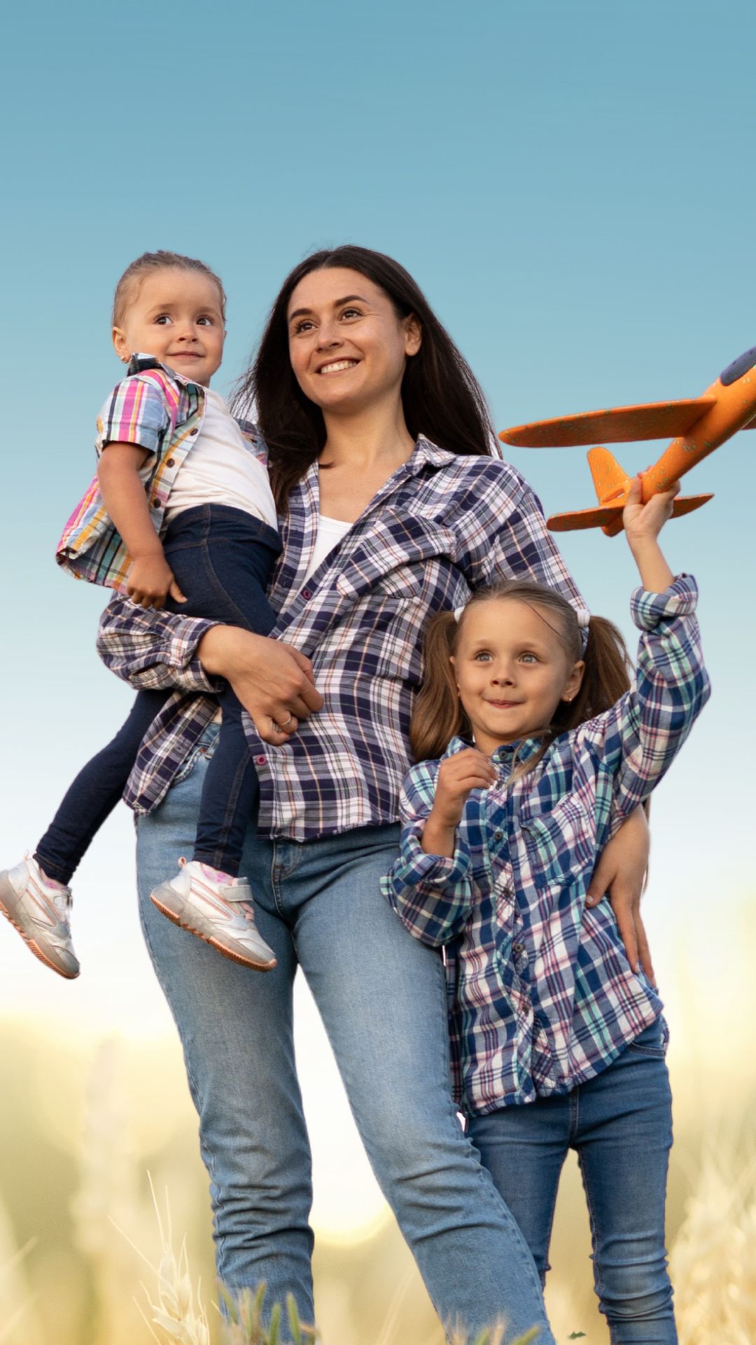 Image of mother and 2 daughters smiling under a blue sky